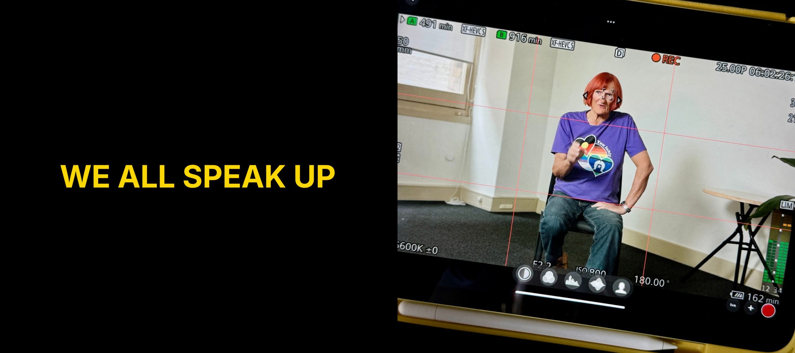 Rainbow Rights campaign graphic: We all speak up, in yellow text on black, beside a behind the scenes photo of a camera monitor showing a participant seated against a plain background, framed full body for filming.